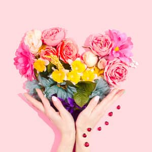 Ein Paar Hände halten einen leuchtenden Blumenstrauß vor einem rosa Hintergrund zum Valentinstag.